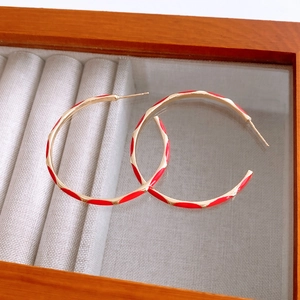 Detail of red and gold enamel hoop earrings with geometric texture in a jewelry box