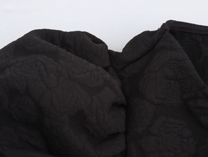Detailaufnahme eines schwarzen Kleides mit floraler Prägung und hochwertigem Stoff