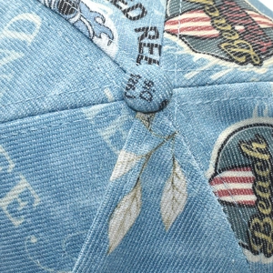Detail of blue denim baseball cap showing vintage beach print and top button stitching