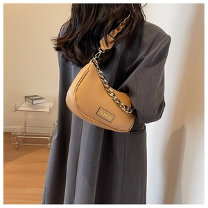 Detail of brown crescent hobo bag with gold chain strap on a model in a grey suit