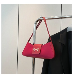 Close-up of a stylish red baguette bag featuring a gold metal bow on a dark jacket