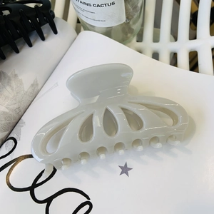 Detailed view of a creamy white petal-shaped hair claw clip on a stylish book background
