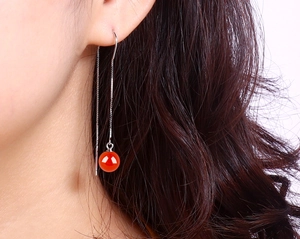 Detailed close-up of a long silver chain earring featuring a vibrant red agate bead drop