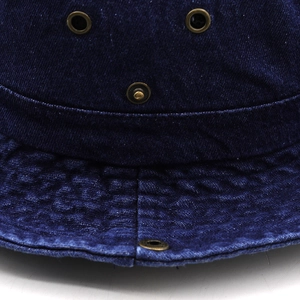 Détail des œillets métalliques et du bouton-pression sur un bob en jean bleu marine texturé