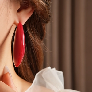 Gros plan d'une grande boucle d'oreille ovale en résine rouge portée par un mannequin