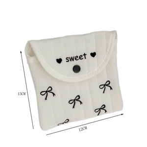 Detail of white quilted sanitary pouch with sweet embroidery and black bow patterns