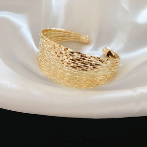 Detail view of a gold multi-layer wide open cuff bracelet with wavy textured metal finish