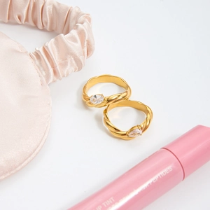 Detailed view of two gold titanium steel rings with white zircons on pink silk background