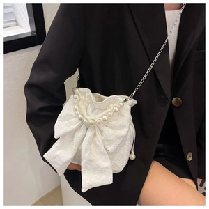 Detail of white fabric bow bag with pearl handle and metal chain on a model