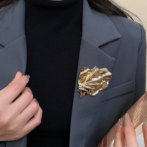 Close-up of a gold wrinkled leaf brooch pinned on a dark grey blazer lapel