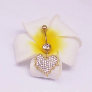 Piercing nombril cœur doré avec cristaux clairs posé sur une fleur de frangipanier
