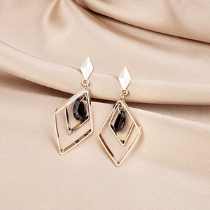 Detailed shot of golden geometric diamond earrings with black teardrop crystals on silk