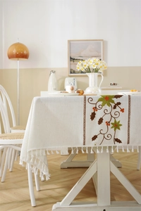 Detail of floral embroidery on beige linen tablecloth with elegant white fringe tassels