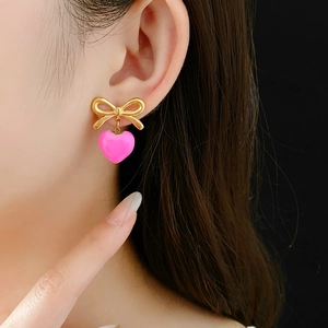Gros plan d'une boucle d'oreille nœud doré avec un pendentif cœur en émail rose vif