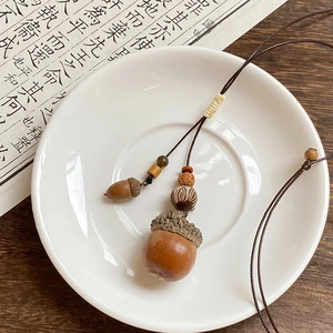 Detailed view of an acorn pendant on a brown woven cord displayed on a ceramic dish