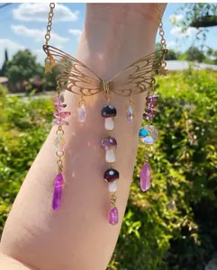 Detail of a butterfly suncatcher with purple crystals and mushroom charms in golden finish
