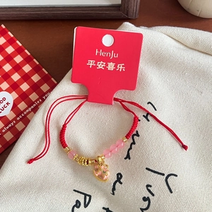 Detail of red braided bracelet with pink glass beads and golden pony charm on canvas bag