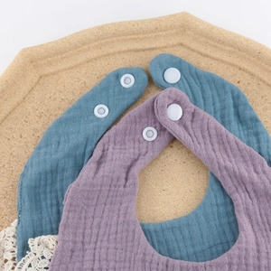 Detail of teal and purple muslin cotton baby bibs with snap buttons on a cork tray