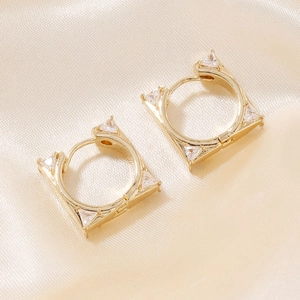 Makro-Detail goldener geometrischer Huggie-Ohrringe mit Zirkonia-Steinen auf Seide