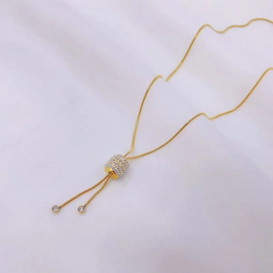 Macro shot of gold snake chain with a cylindrical rhinestone pendant on white silk fabric