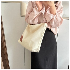 Close-up of beige canvas crossbody bag with brown leather logo detail on model