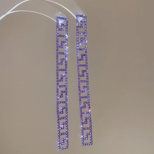 Dettaglio di orecchini lunghi in argento con strass viola e motivi geometrici a chiave greca