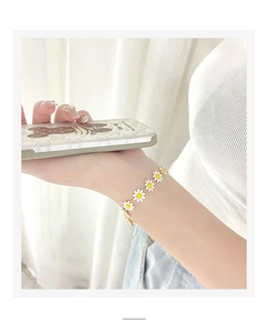 Detail of daisy bracelet with white petals and gold chain worn on a female wrist
