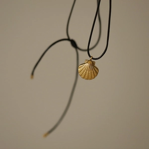 Close-up of golden shell pendant necklace with black braided rope and steel accents