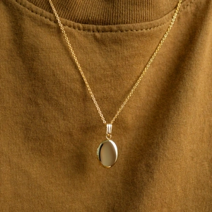 Close-up of polished 18K gold oval locket pendant necklace worn on a brown fabric