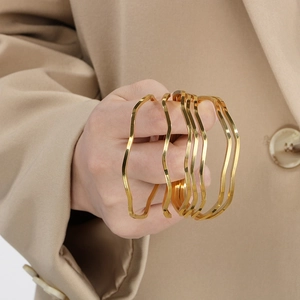 Detailed close-up of five layered wave-shaped gold bracelets in polished titanium steel