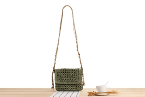 Close-up of a dark green woven crossbody bag with wooden bead strap on a wooden surface