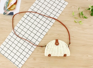 Detailed view of semi-circular straw crossbody bag with white weaving and brown leather trim