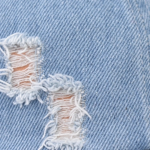 Detailed macro view of distressed light blue denim fabric with frayed hole texture