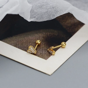 Macro shot of gold V-shaped stud earrings with rectangular zircons on artistic background