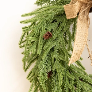 Détail d'une couronne de Noël avec aiguilles de pin, cônes et nœud en toile de jute
