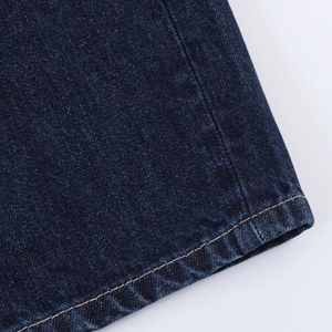 Détail de l'ourlet en denim bleu foncé montrant la double couture précise sur le tissu