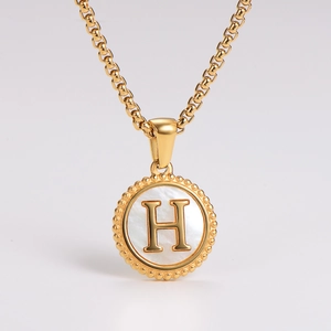 Detailed shot of gold-plated pendant necklace with white shell inlay and letter H