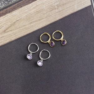 Detail of silver and gold hoop earrings featuring vibrant purple cubic zirconia stones