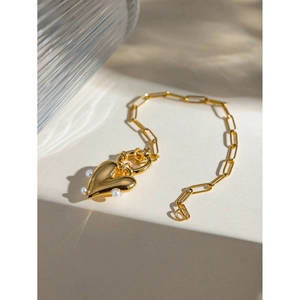 Detail of 18k gold paperclip chain bracelet with a heart pendant and small pearls