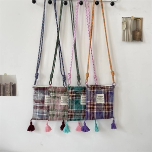 Detailed view of four plaid tassel crossbody phone bags hanging on a white wall