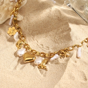 Vue détaillée du bracelet en chaîne dorée avec perles et charms sur fond de sable