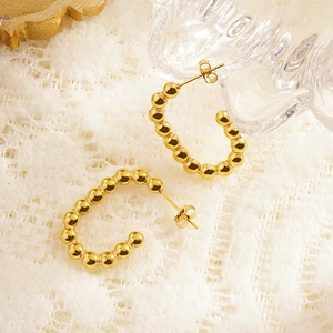 Detailed close-up of golden beaded C-shape earrings on elegant white lace background