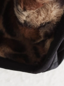 Close-up of fluffy leopard faux fur lining and black fabric texture on bomber jacket