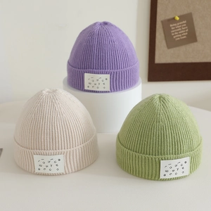 Three candy-colored knit beanies in purple, beige and green with stylish letter patch
