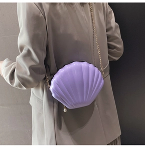 Detail view of purple shell-shaped evening bag with gold chain strap and pearl charm
