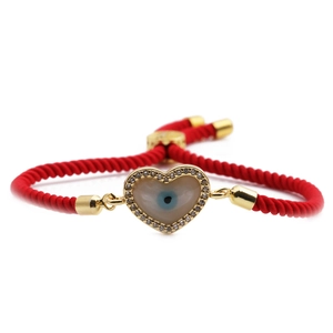 Adjustable red braided heart bracelet with golden evil eye zircon pendant on white background