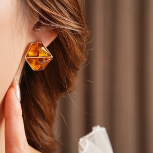 Close-up of a geometric amber resin earring with a gold frame on wavy brown hair