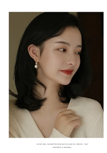 Detail view of double white freshwater pearls on golden drop earrings worn by a model