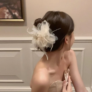 Close-up of elegant cream fabric flower hair claw with feathers and beads on a hair bun
