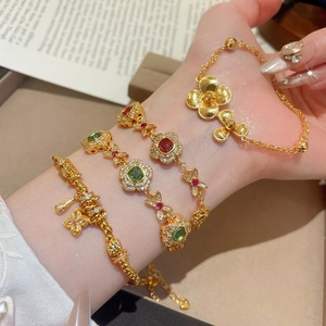 Detail of 24K gold plated bracelets featuring floral motifs and clover charm on wrist